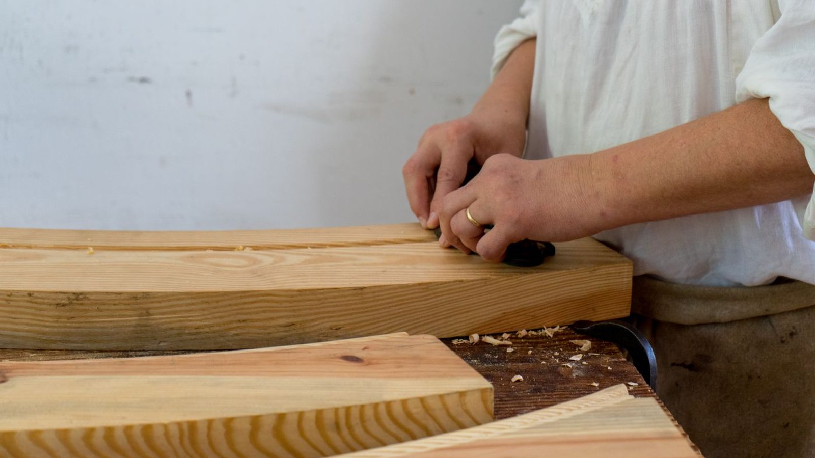 Hands smoothing a length of timber with a hand plane at a workbench